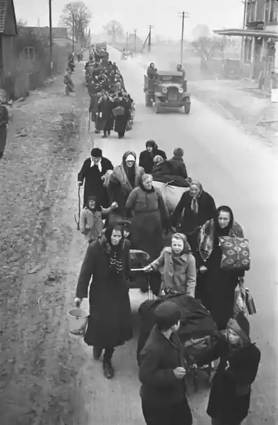 A long column of women, children and men with bundles and handcarts along a country road.